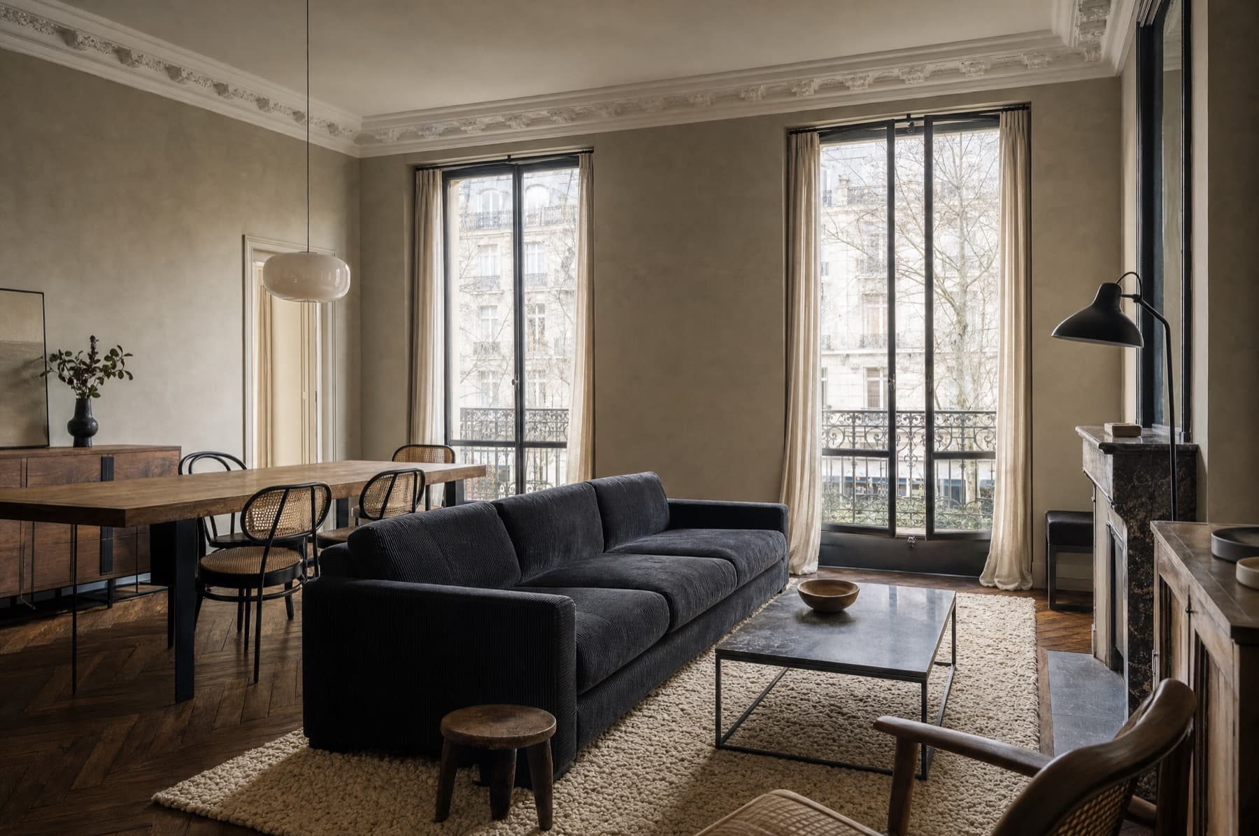 Séjour d'un appartement haussmannien : canapé trois places, table de repas en chêne, chaises cannées, tapis de laine et suspension en verre opalin