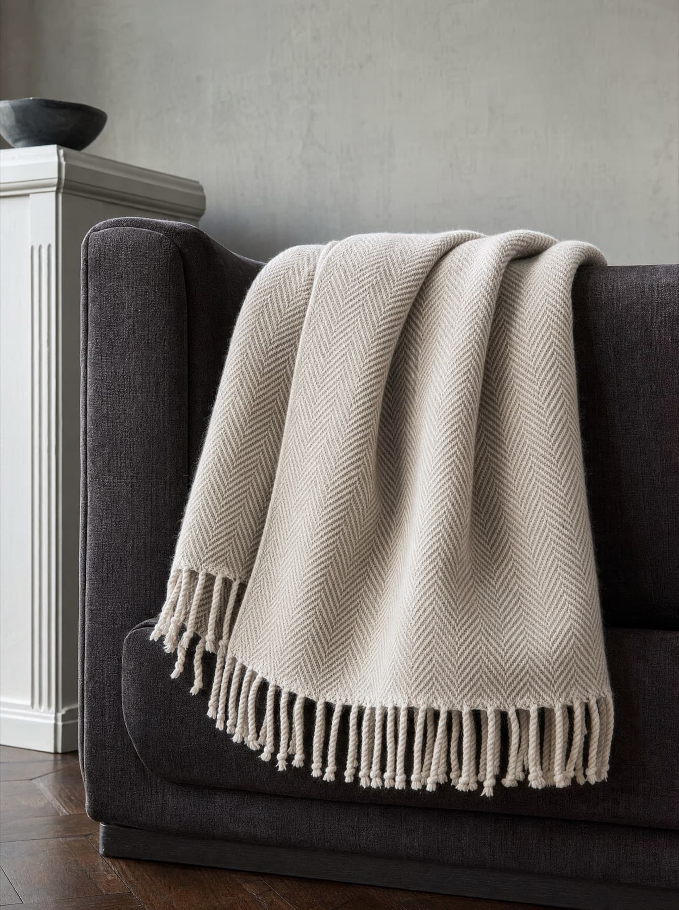 Plaid Aubrac en laine mérinos écrue plié sur l’accotoir d’un fauteuil, tissage chevron et franges nouées