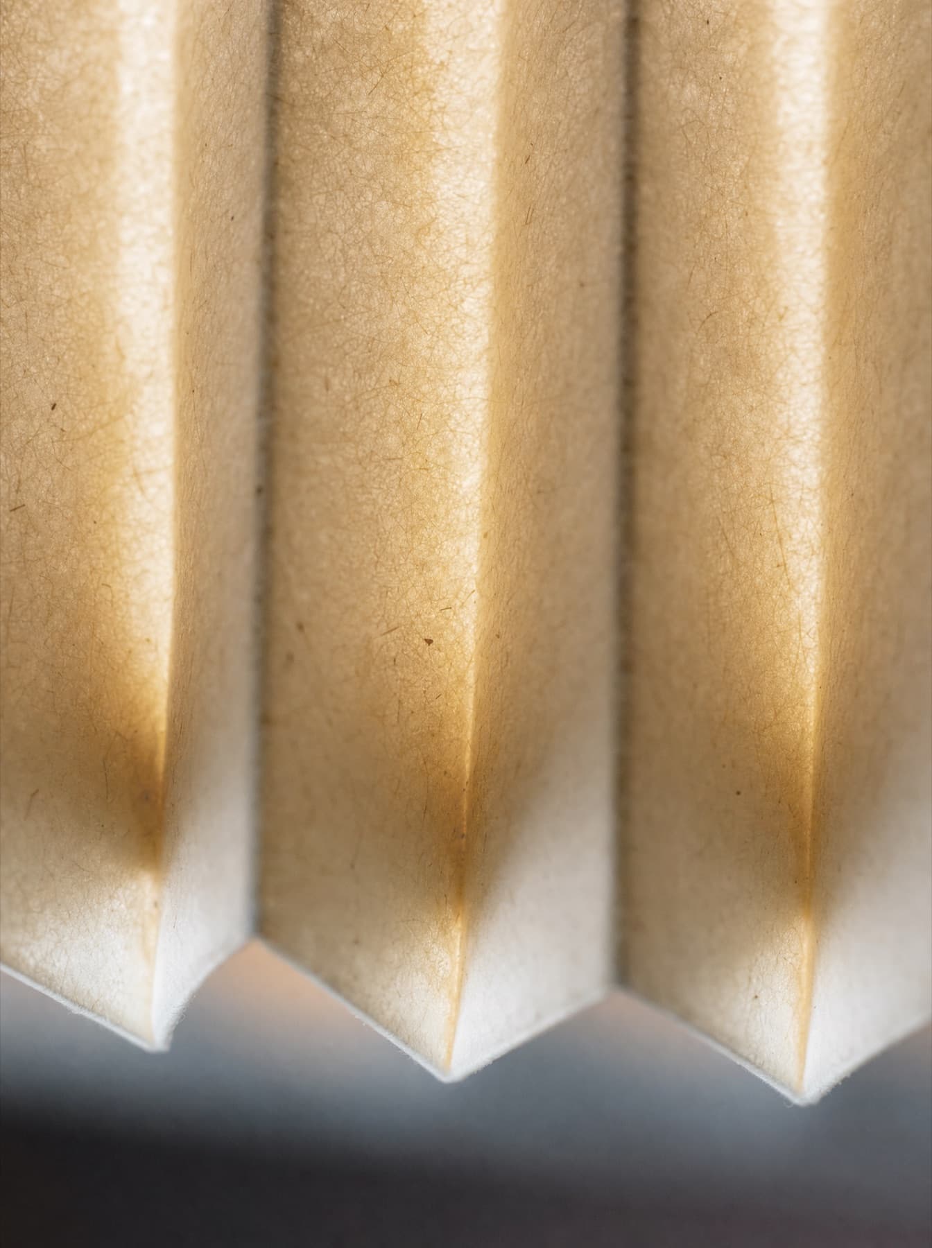 Détail du papier plissé de la suspension Ouessant à contre-jour : la fibre transparaît, les arêtes de pli portent une ombre fine