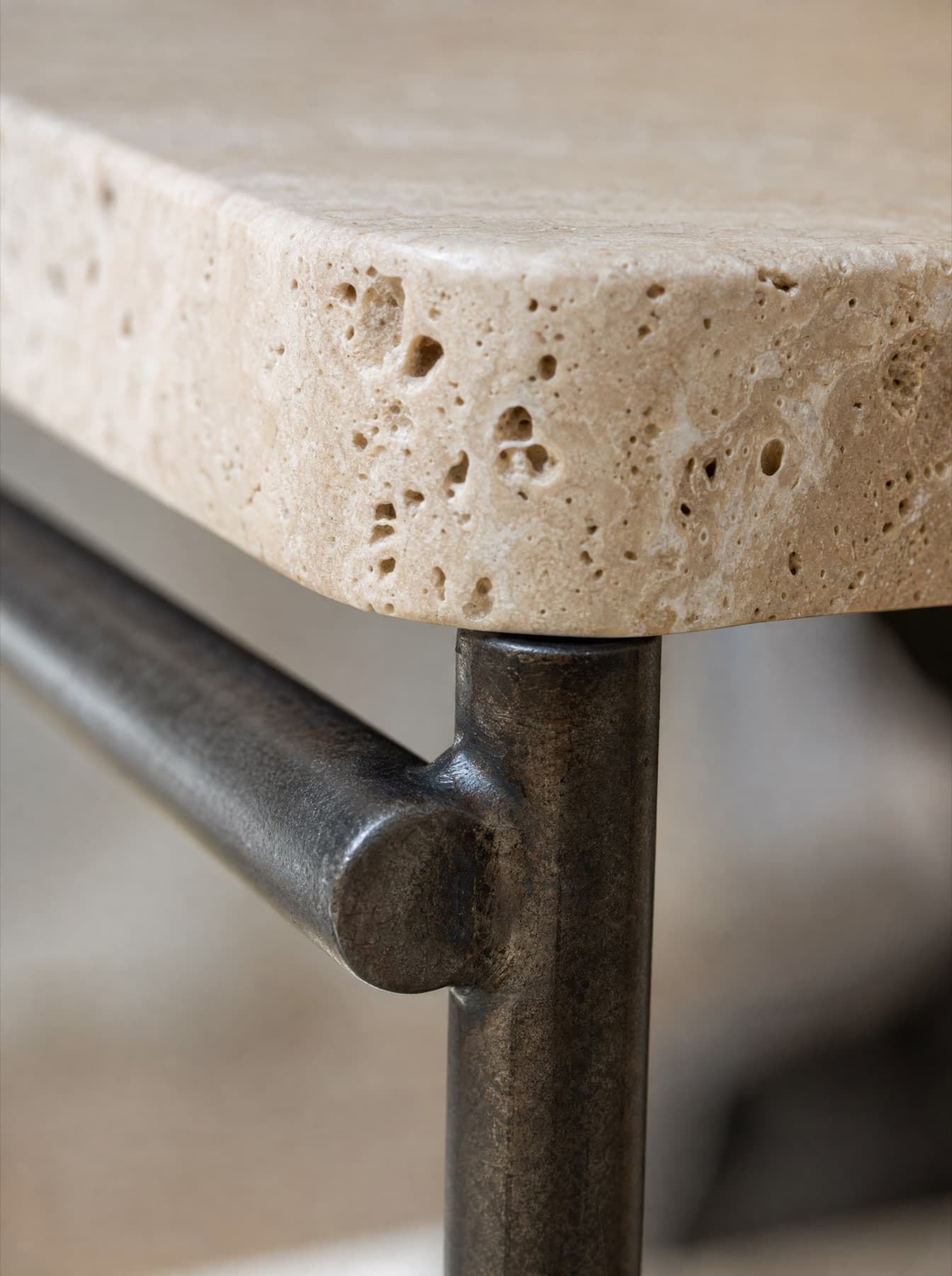 Détail de la table Sienne : le chant du travertin avec ses vides naturels et la soudure du tube d’acier sous le plateau