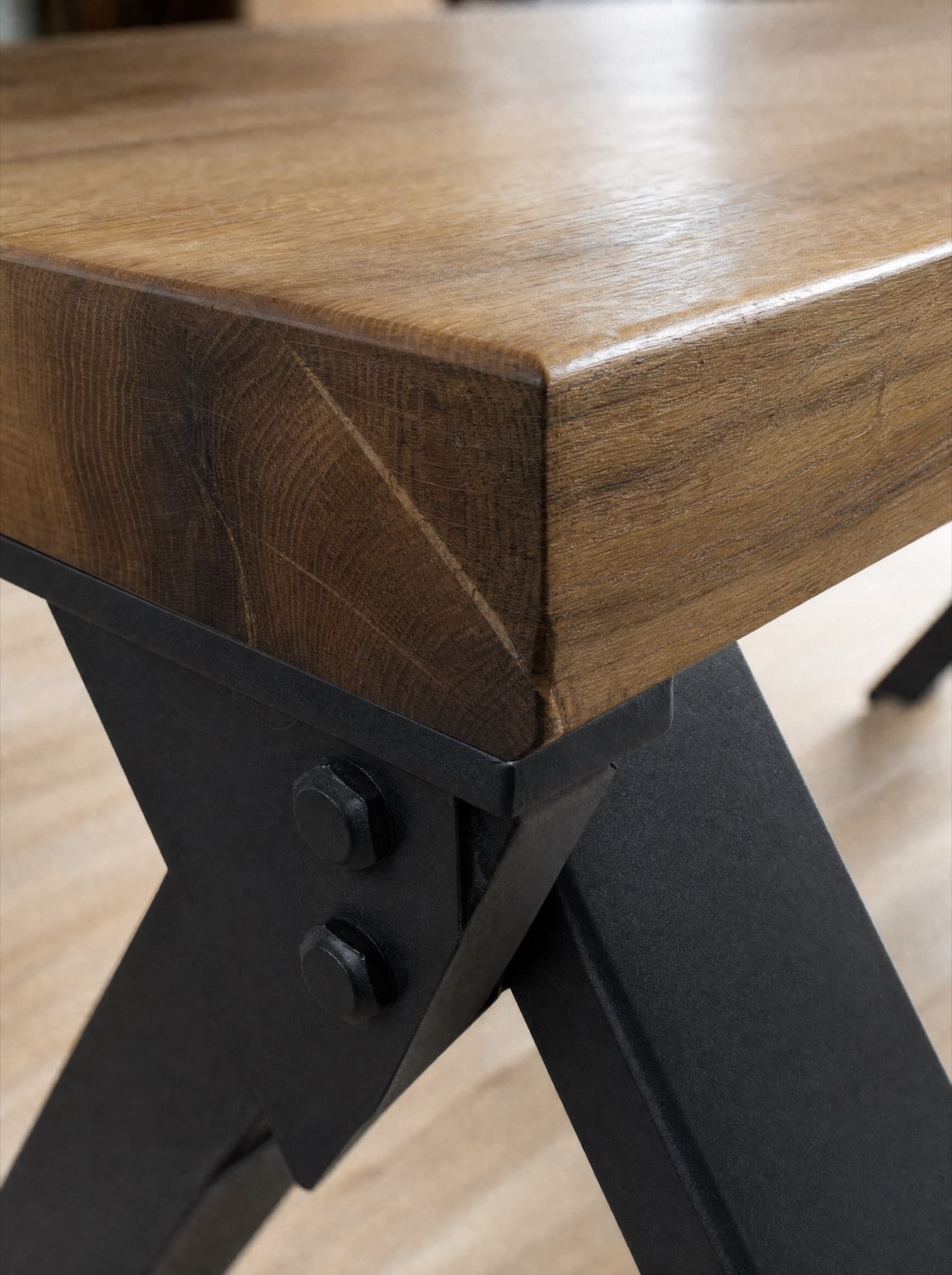Détail de la table Garonne : l’angle du plateau de chêne huilé, le chant chanfreiné et l’assemblage boulonné du tréteau d’acier
