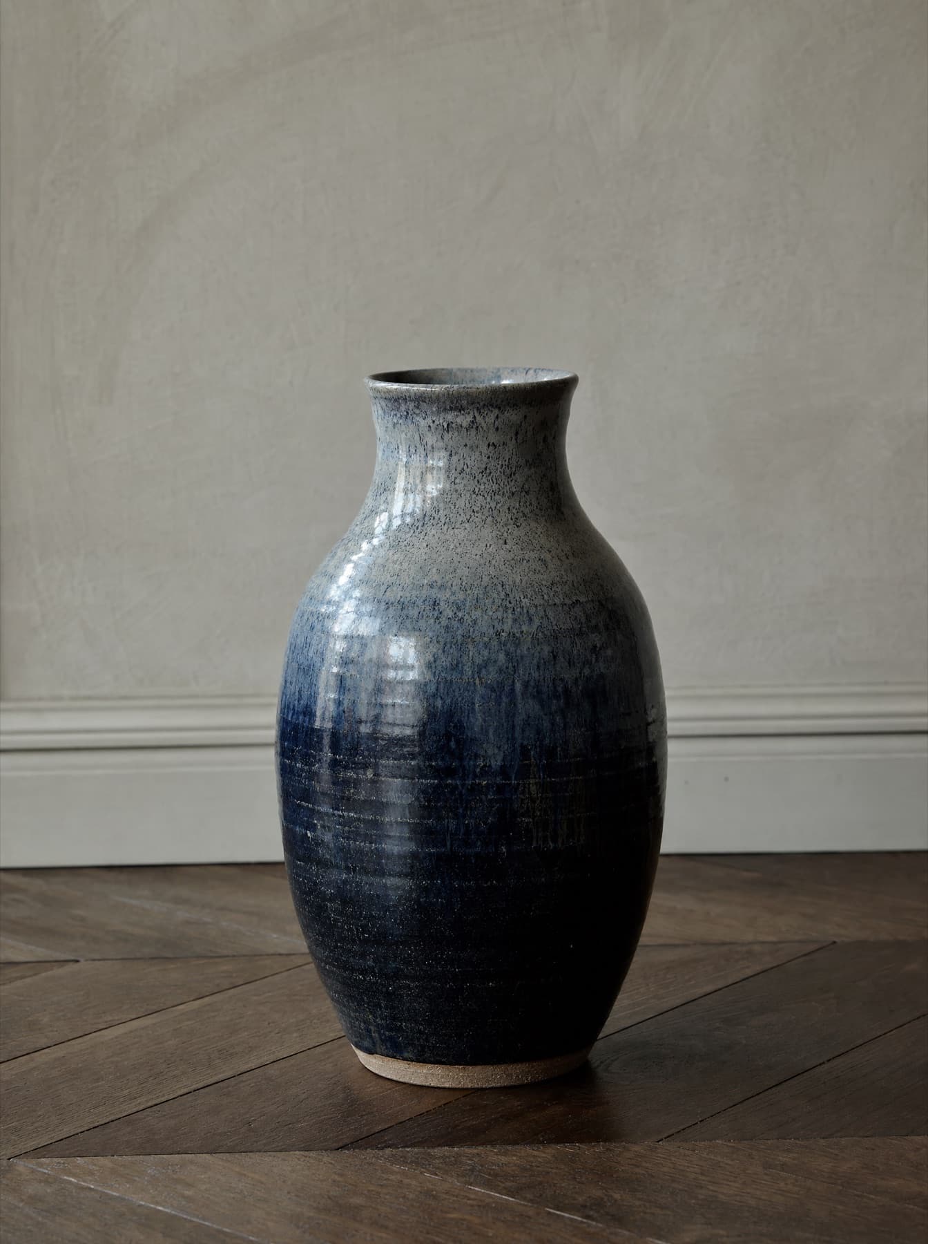 Vase Ravenne posé sur un parquet de chêne sombre, épaule renflée et col resserré, émail réactif qui coule du bleu nuit au gris moucheté
